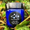 CBD Skin Balm on a background of ivy plant in a blue jar with a black lid.