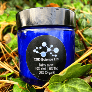 CBD Skin Balm on a background of ivy plant in a blue jar with a black lid.