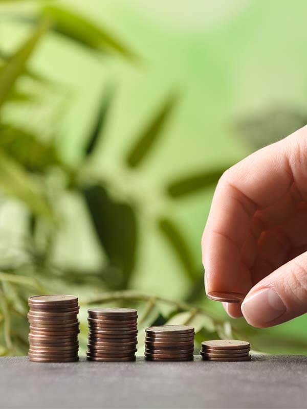 4 stacks of copper coins being stacked by a hand. Green pant background.